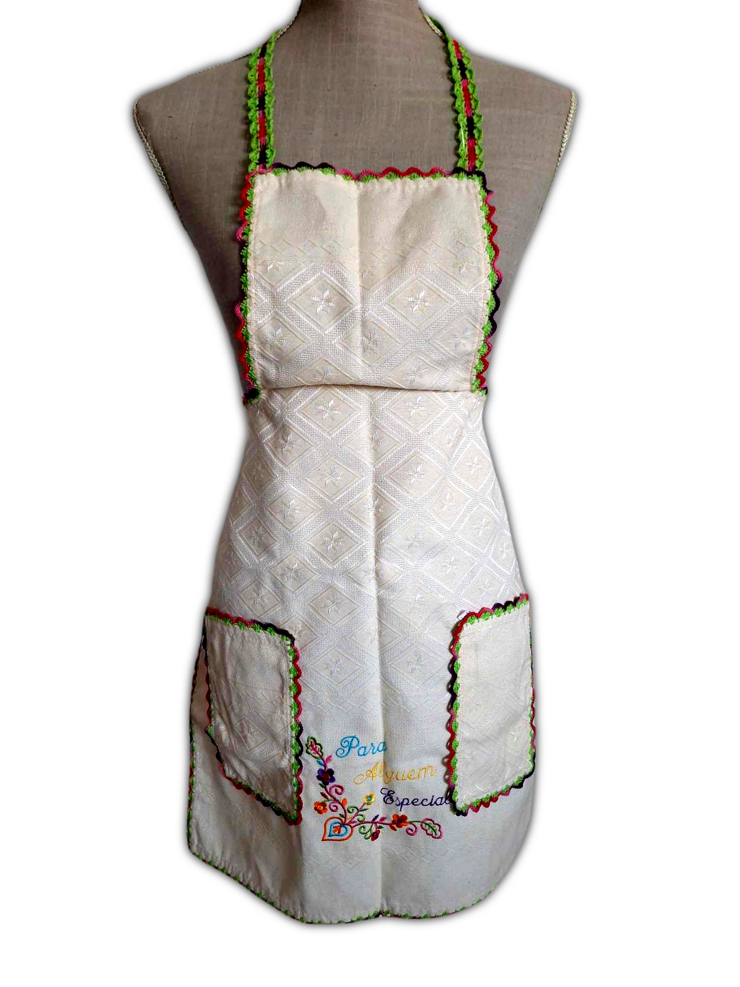 Avental de tecido bege 100% algodão, com picô colorido a toda a volta. Este tem ainda dois bolsos na parte da frente, também com o mesmo picô e um bordado decorativo entre os bolsos.