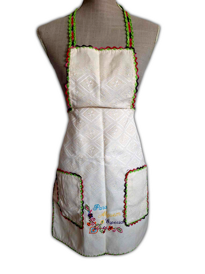 Avental de tecido bege 100% algodão, com picô colorido a toda a volta. Este tem ainda dois bolsos na parte da frente, também com o mesmo picô e um bordado decorativo entre os bolsos.