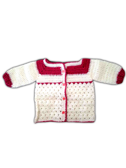 O casaco de bebé é inteiramente branco, com uma textura delicada e uniforme de crochê. As bordas da peça, incluindo a gola, os punhos e a abertura frontal, são cuidadosamente contornadas com um fio rosa forte, criando um contraste vibrante e encantador. As mangas são compridas e a parte da frente conta com pequenos botões que permitem o fecho do casaco.