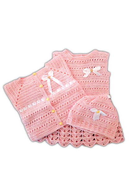 Conjunto de bebé com três peças em tom rosa suave. O casaquinho tem um lacinho decorativo à frente e detalhes rendados nas mangas e na bainha. Inclui também um vestido e um gorro a condizer com acabamento delicado.