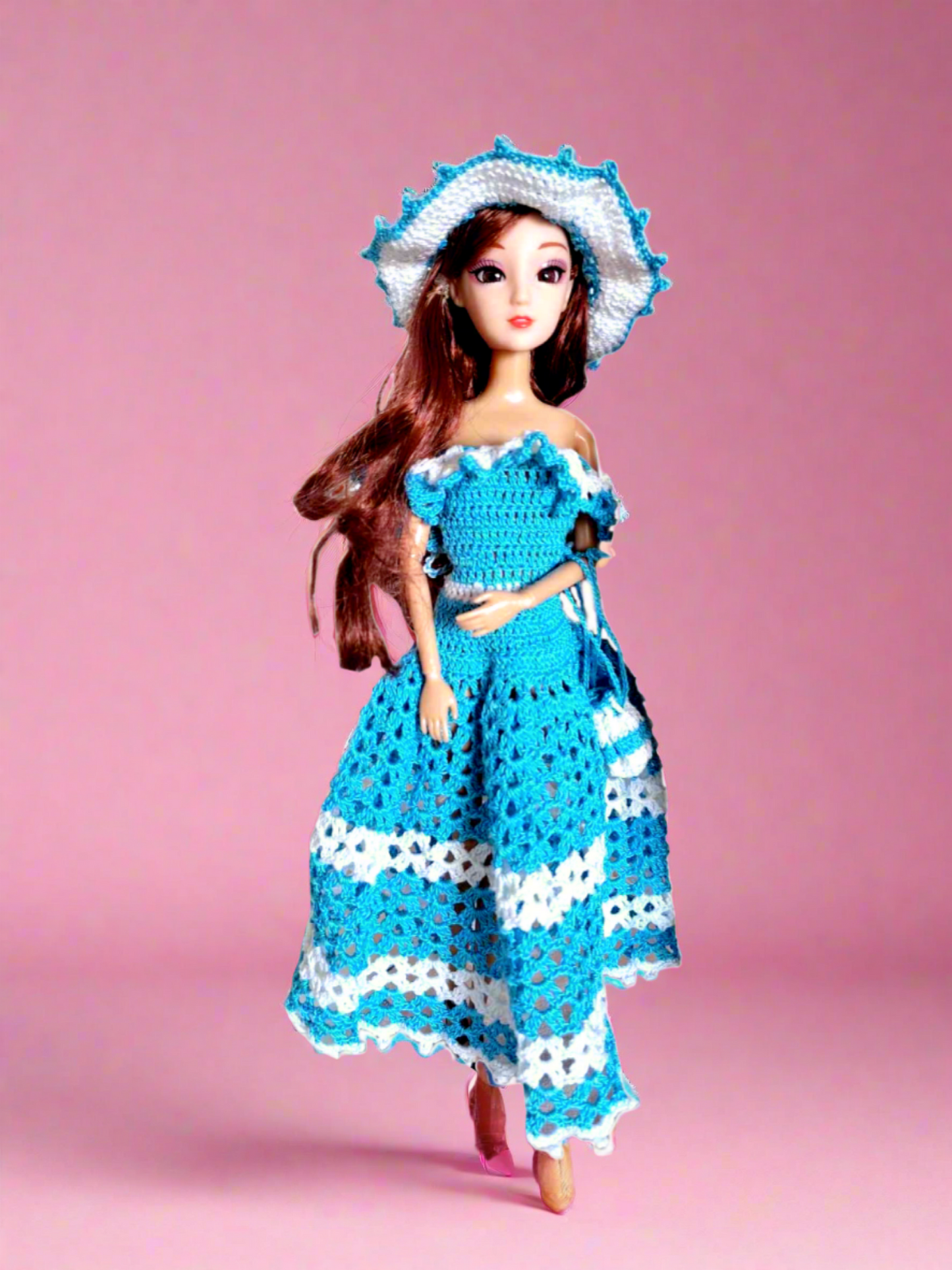 Vista frontal do vestido, maioritariamente azul, com alguns pormenores em branco como os folhos que caem a volta dos ombros e duas faixas na saia, uma a meio e outra no fundo. Tem ainda como acessórios um bonito chapéu e uma pequena bolsa ambos com a mesmas cores do vestido. 