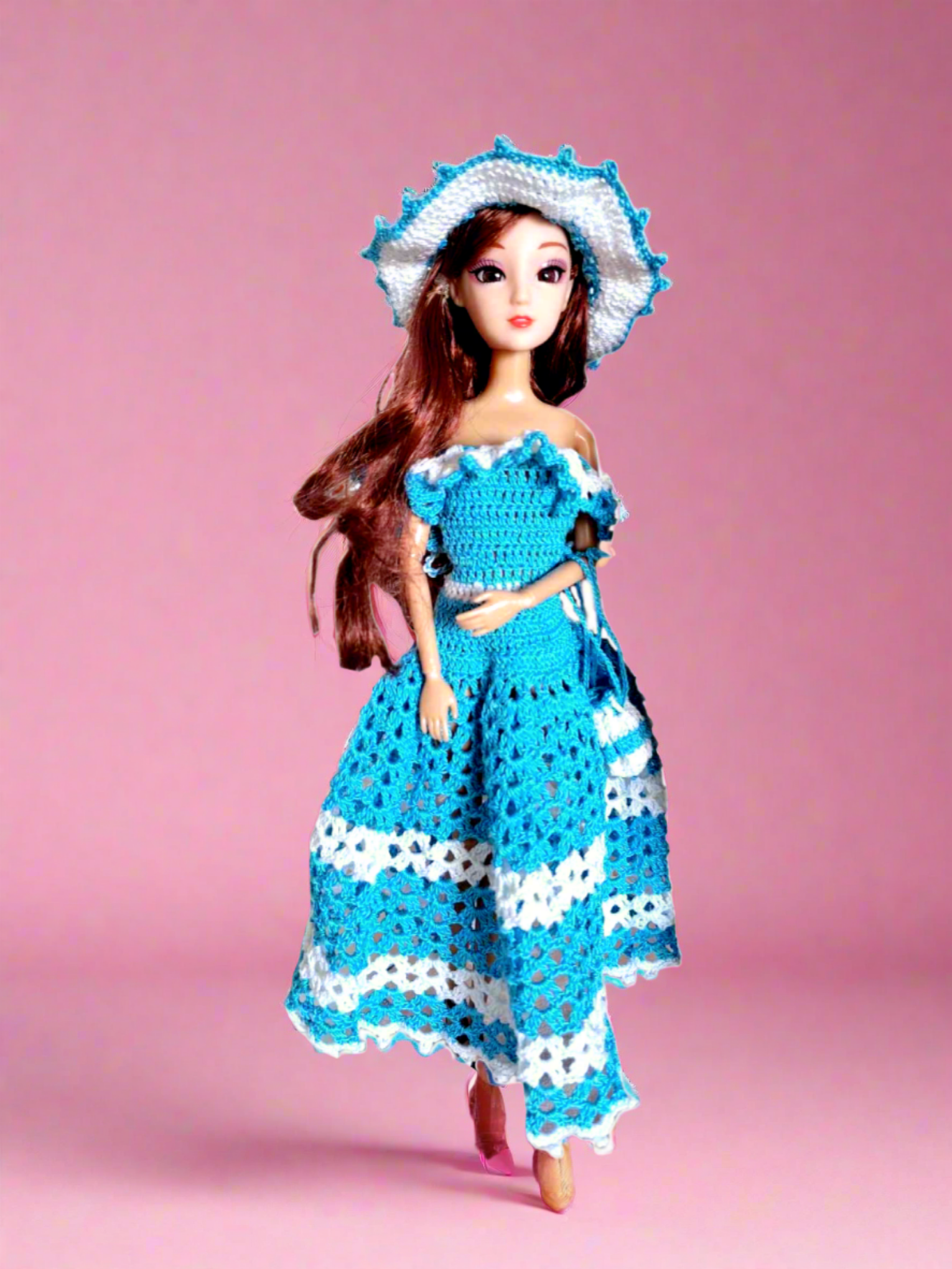 Vista frontal do vestido, maioritariamente azul, com alguns pormenores em branco como os folhos que caem a volta dos ombros e duas faixas na saia, uma a meio e outra no fundo. Tem ainda como acessórios um bonito chapéu e uma pequena bolsa ambos com a mesmas cores do vestido. 