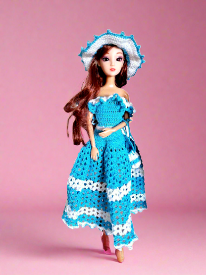 Vista frontal do vestido, maioritariamente azul, com alguns pormenores em branco como os folhos que caem a volta dos ombros e duas faixas na saia, uma a meio e outra no fundo. Tem ainda como acessórios um bonito chapéu e uma pequena bolsa ambos com a mesmas cores do vestido. 
