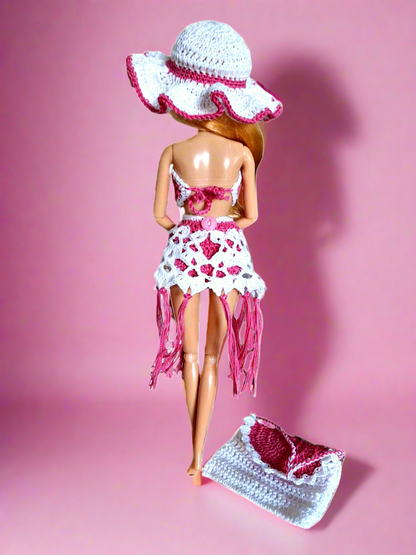 Aqui temos novamente a vista da parte de trás do conjunto, mas neste caso destaca-se o pormenor do pequeno botão cor de rosa que serve para apertar a saída de praia. Temos ainda a mala que está no chão onde se pode ver que esta é toda branca com a exceção da aba e da alça. 