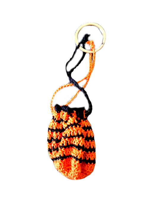 Este porta chaves é na forma de uma pequena bolsinha, maioritariamente laranja e com alguns detalhes em preto. Tem fios compridos que servem para fechar a sua abertura, podendo assim usa lo como um pequeno porta moedas.