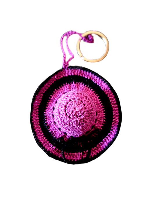 Porta Chaves no formato de um elegante chapéu. Este é maioritariamente roxo com alguns pormenores em preto e ainda um fio que dá a volta ao centro do chapéu para o adornar com um bonito laço.