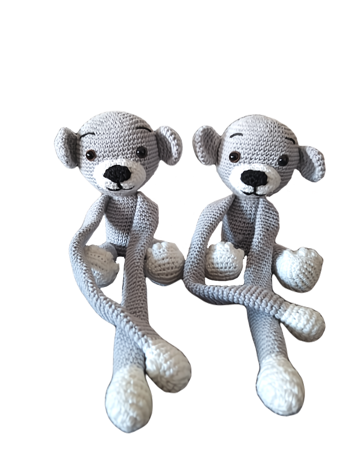 Par de macaquinhos de crochet cinzentos com patas e focinhos brancos, sentados lado a lado. Têm braços e pernas compridos, olhos pretos e expressão simpática.