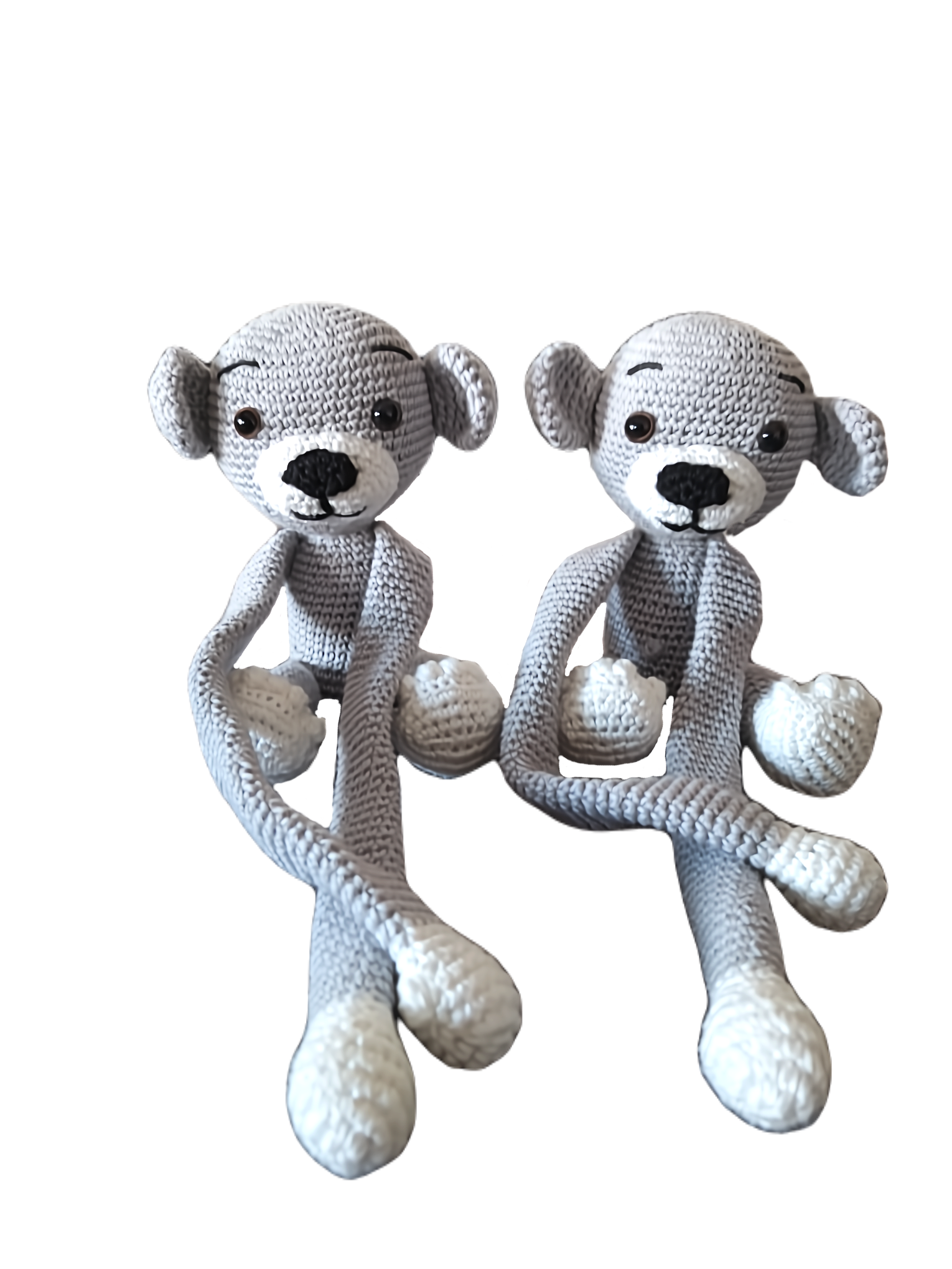 Par de macaquinhos de crochet cinzentos com patas e focinhos brancos, sentados lado a lado. Têm braços e pernas compridos, olhos pretos e expressão simpática.