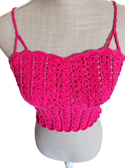 Vista superior aproximada de um top de crochet fúcsia num manequim, focando as copas em forma de conchas. O ângulo destaca o relevo e a curvatura do design, realçando o efeito de concha criado com pontos detalhados.