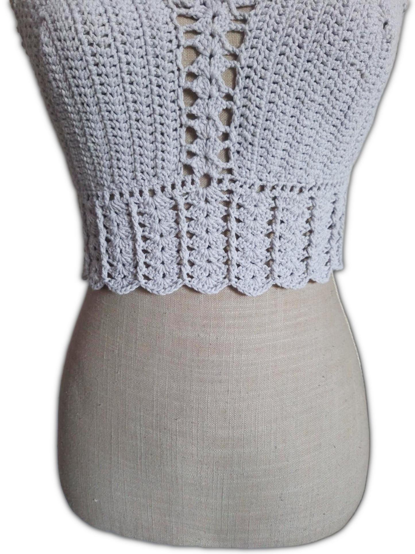 Close-up da parte inferior de um top de crochet branco. Mostra o detalhe do acabamento com ponto de conchas, revelando a textura delicada e o trabalho artesanal dos pontos.