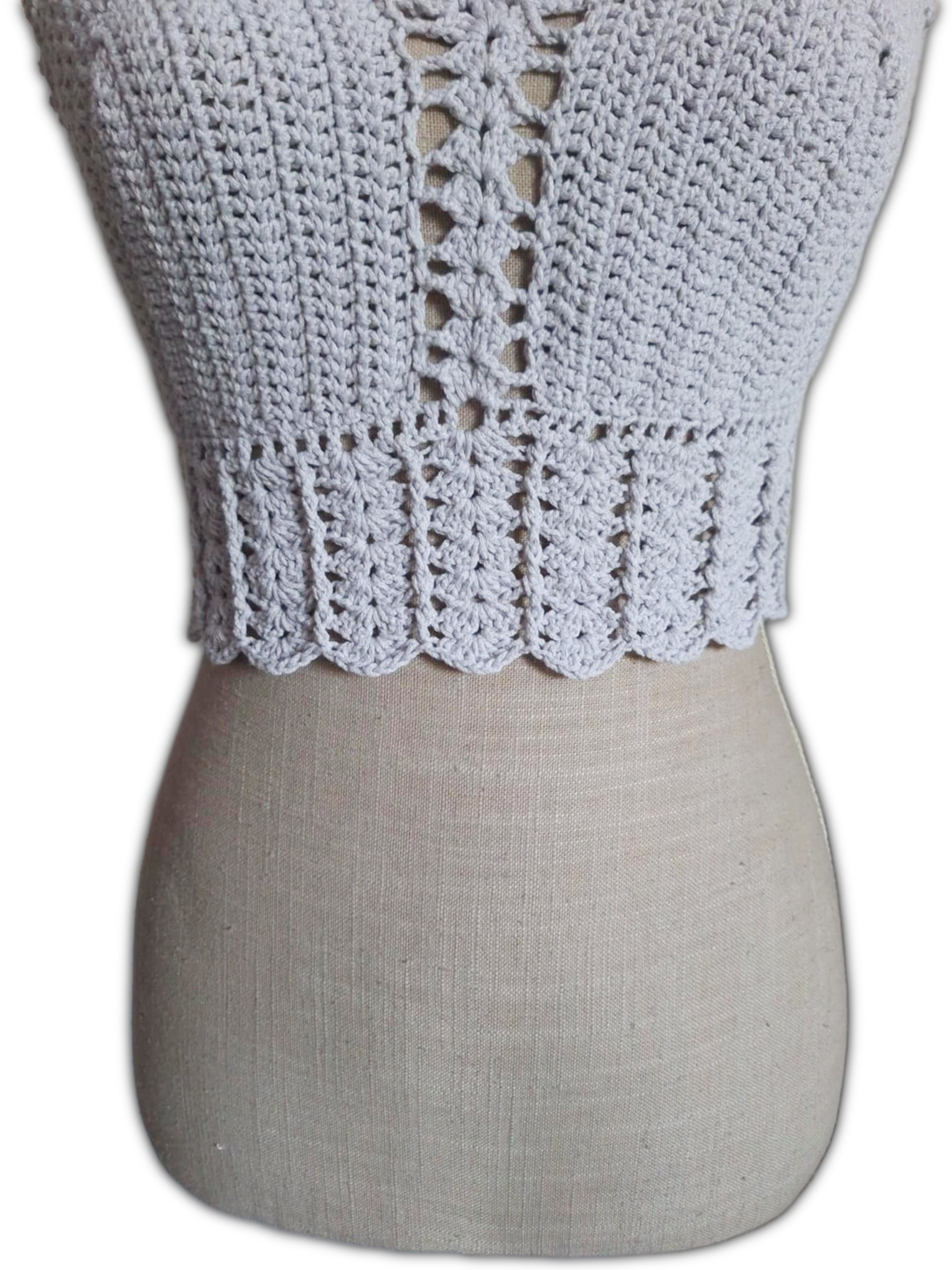Close-up da parte inferior de um top de crochet branco. Mostra o detalhe do acabamento com ponto de conchas, revelando a textura delicada e o trabalho artesanal dos pontos.