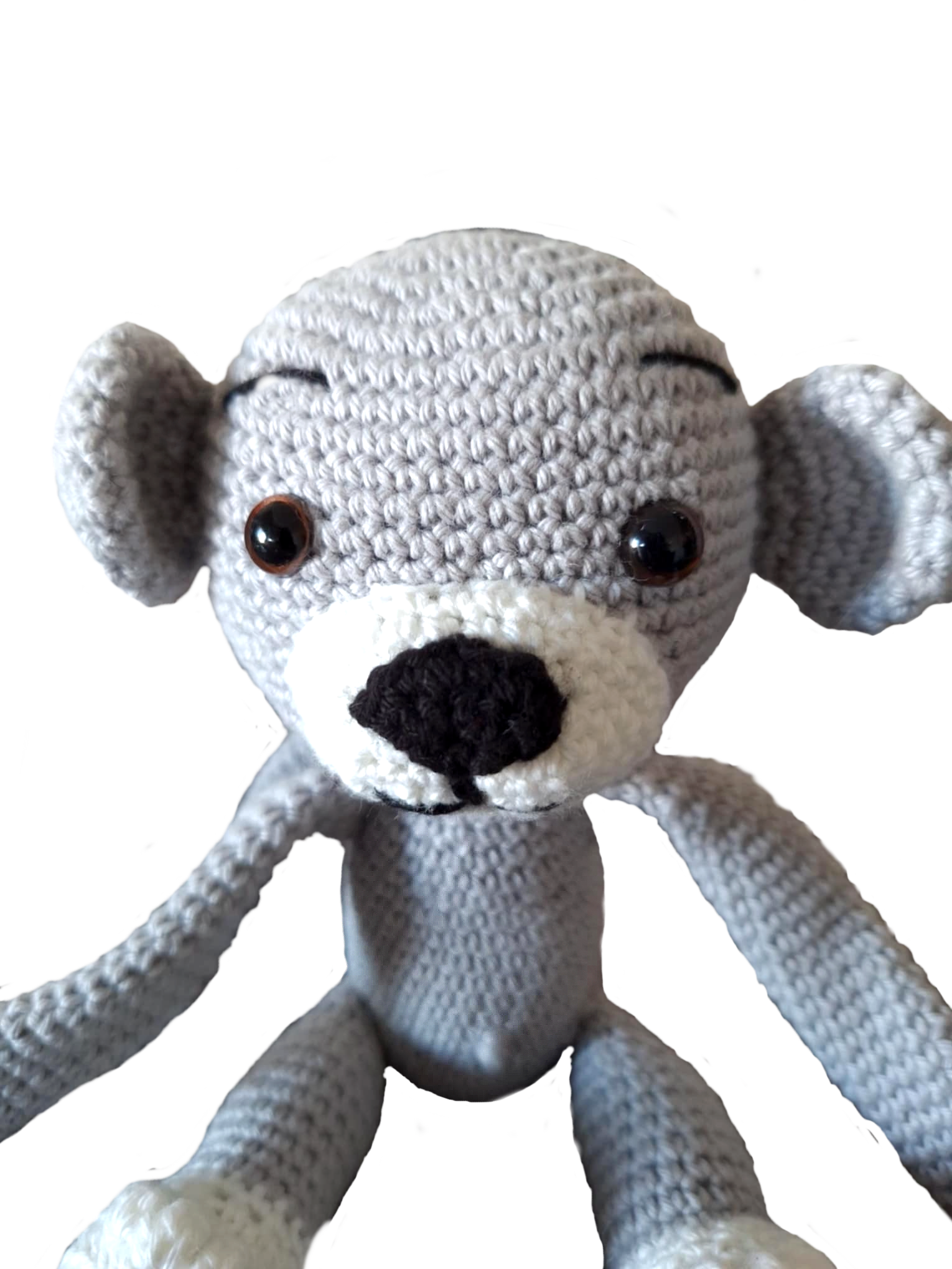 Close-up do rosto de um macaquinho de crochet cinzento. Mostra em detalhe os olhos castanhos de segurança, o nariz preto bordado, o focinho branco e a expressão simpática. A textura do crochet é visível, com pontos pequenos e uniformes.
